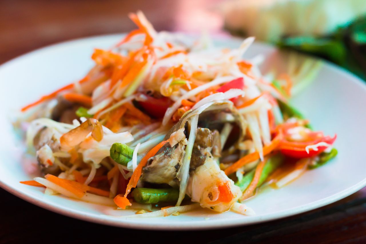 about-us-02 Close-up of a vibrant Thai papaya salad with fresh vegetables and herbs.
