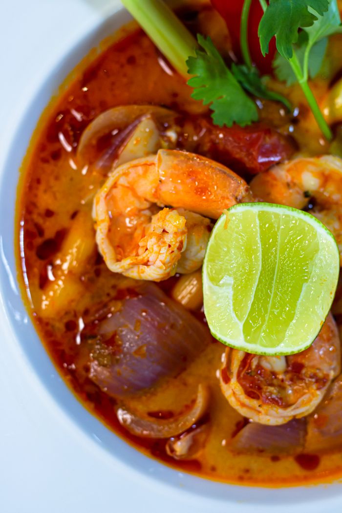 about-us-02 Authentic Thai Tom Yum soup with shrimp, lime, and herbs in a rich broth, showcasing vibrant flavors and colors.
