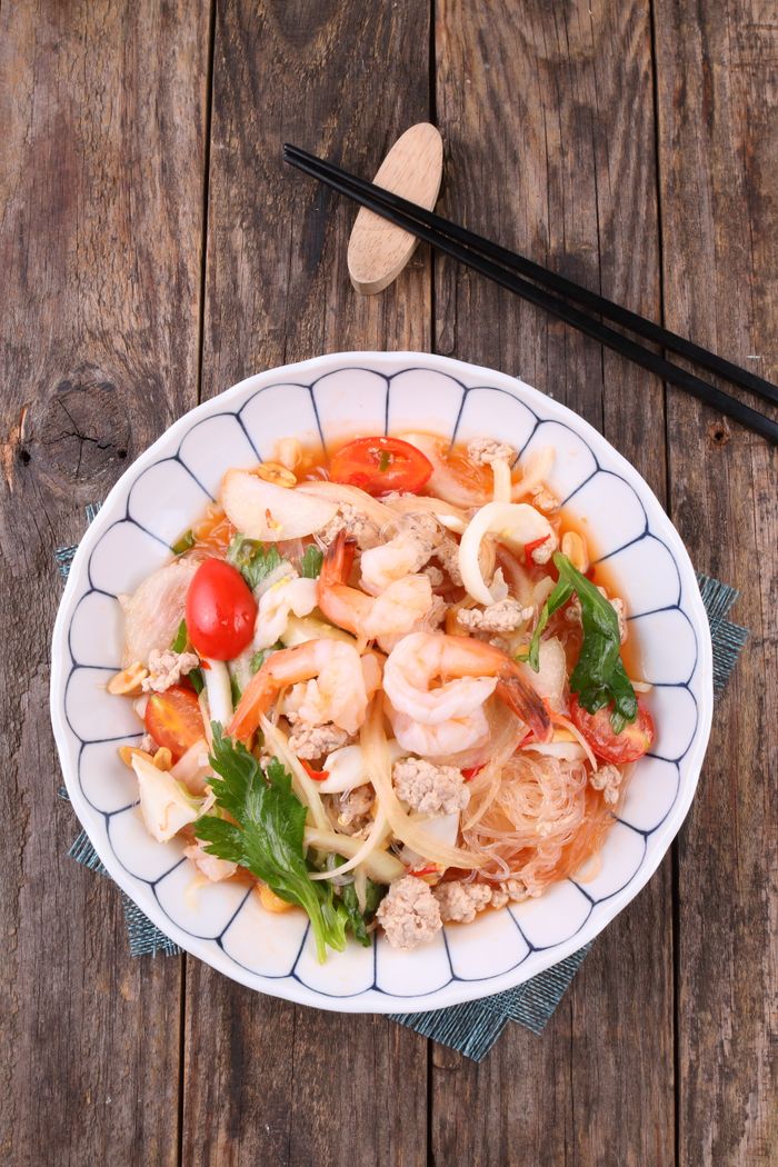 services-03 Appetizing Thai glass noodle salad topped with fresh seafood on a rustic wooden table.